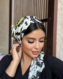 A woman wearing a headscarf and black top, exuding elegance and grace.
